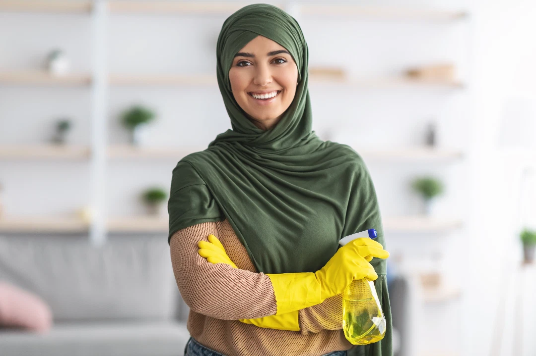 Live-out maid cleaning a Dubai apartment kitchen with Marina skyline visible through the window